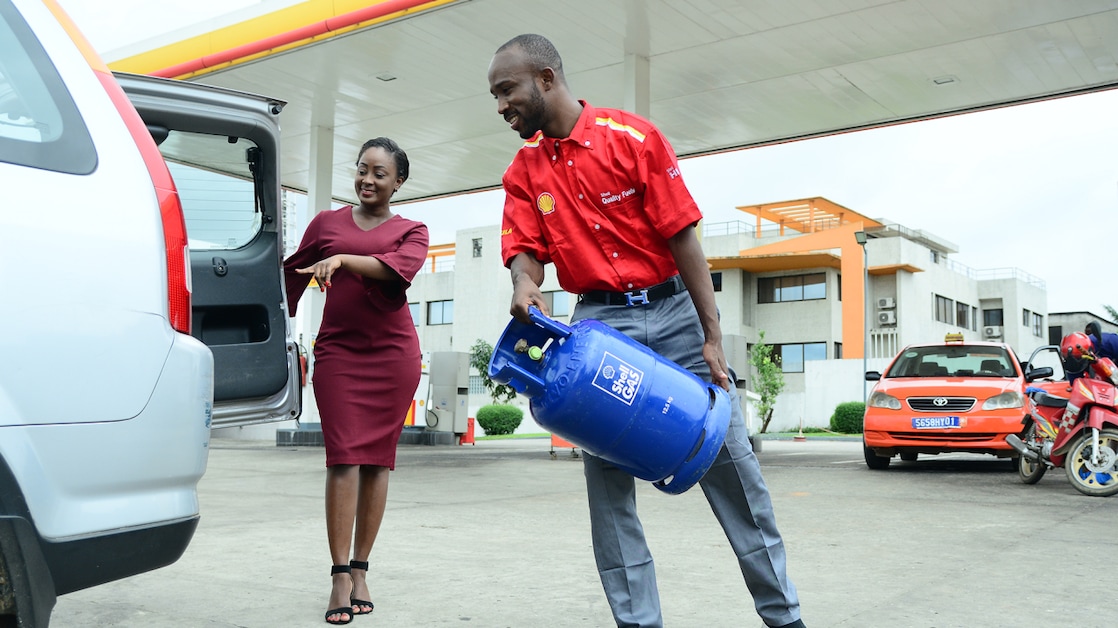 Un employé de Shell met une bouteille Shell Gas dans le coffre d'une cliente.