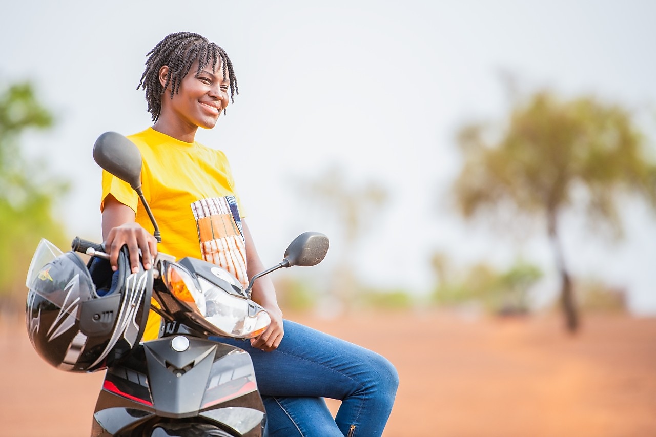 Moto rouge et conducteur sur une route avec des voitures et des bâtiments dans l’arrière-plan.